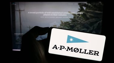 Stuttgart, Almanya - 09-19-2023: Danimarkalı A.P. şirketinin logosuyla cep telefonu tutan kişi Moller Holding AS (APMH) web sayfasının önünde ekranda. Telefon ekranına odaklan.