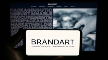 Stuttgart, Germany - 09-20-2023: Person holding smartphone with logo of Italian packaging company Brandart  S.p.A. on screen in front of website. Focus on phone display. clipart