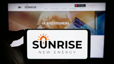 Stuttgart, Germany - 09-20-2023: Person holding smartphone with logo of Chinese company Sunrise New Energy Co. Ltd. on screen in front of website. Focus on phone display. clipart