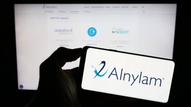 Stuttgart, Almanya - 09-20-2023: ABD 'li şirket Alnylam Pharmaceuticals Inc.' in logosuyla cep telefonu sahibi kişi iş sayfasının önünde ekranda. Telefon ekranına odaklan.