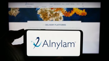 Stuttgart, Almanya - 09-20-2023: ABD 'li Alnylam Pharmaceuticals Inc. şirketinin logosunu elinde tutan kişi web sitesinin önünde ekranda. Telefon ekranına odaklan.