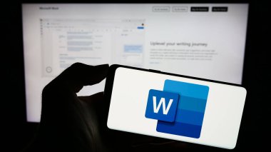 Stuttgart, Almanya - 09-21-2023: Kelime işleme yazılımı logosu olan cep telefonu sahibi kişi Microsoft Word iş sayfasının önünde ekranda. Telefon ekranına odaklan.