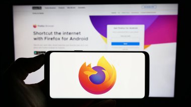 Stuttgart, Almanya - 09-22-2023: İnternet sayfasının önündeki ekranda açık kaynak web tarayıcısı Mozilla Firefox logosu olan cep telefonu sahibi kişi. Telefon ekranına odaklan.