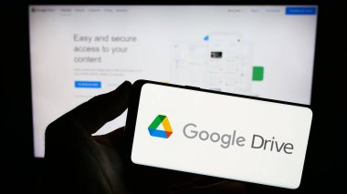 Stuttgart, Almanya - 09-22-2023: Web sitesinin önündeki ekranda Google Drive dosya depolama platformunun logosuna sahip akıllı telefonu tutan kişi. Telefon ekranına odaklan.