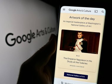 Stuttgart, Germany - 09-23-2023: Person holding cellphone with webpage of online platform Google Arts and Culture on screen in front of logo. Focus on center of phone display. clipart