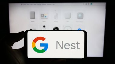 Stuttgart, Almanya - 09-23-2023: Akıllı ev platformu Google Yuvası logosuna sahip cep telefonu sahibi kişi iş sayfasının önünde ekranda. Telefon ekranına odaklan.