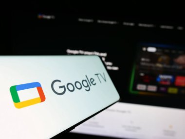 Stuttgart, Almanya - 09-23-2023: İş dünyasının web sitesinin önündeki ekranda Google TV hizmeti üzerinde video logosu bulunan akıllı telefon. Telefon ekranının soluna odaklan.