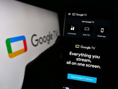 Stuttgart, Almanya - 09-23-2023: Logonun önündeki ekranda Google TV servisini talep eden bir web sayfası üzerinde cep telefonu bulunan kişi. Telefon ekranının merkezine odaklan.