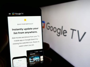 Stuttgart, Almanya - 09-23-2023: Logonun önündeki ekranda Google TV servisini talep eden video web sayfası ile akıllı telefon tutan kişi. Telefon ekranının merkezine odaklan.