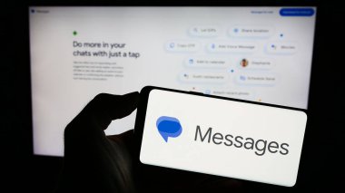 Stuttgart, Almanya - 09-23-2023: Cep telefonunda anlık mesajlaşma uygulaması logosu olan kişi şirket web sayfasının önünde ekranda Google Mesajları 'nı tutuyor. Telefon ekranına odaklan.