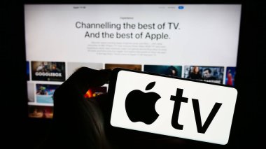 Stuttgart, Almanya - 09-23-2023: Cep telefonunda Apple TV 'nin video yayınlama servisi logosu ve iş dünyasının web sayfası önündeki ekranda bulunan kişi. Telefon ekranına odaklan.