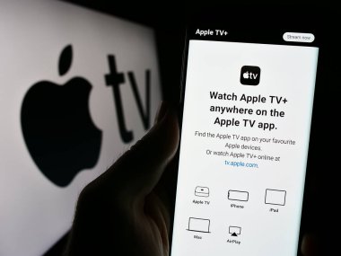 Stuttgart, Almanya - 09-23-2023: Cep telefonunda Apple TV 'nin web sitesi ve logonun önündeki ekranda bulunan kişi. Telefon ekranının merkezine odaklan.
