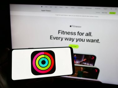 Stuttgart, Almanya - 09-23-2023: Web sitesi önünde ekranda Apple Fitness uygulamasının egzersiz izleme logosuna sahip akıllı telefonu tutan kişi. Telefon ekranına odaklan.