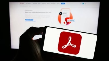 Stuttgart, Almanya - 09-23-2023: PDF yönetim yazılımı Adobe Acrobat 'ın logosu olan cep telefonu sahibi kişi iş sayfasının önünde ekranda. Telefon ekranına odaklan.