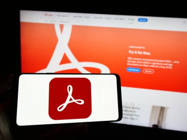 Stuttgart, Almanya - 09-23-2023: PDF yönetim yazılımı Adobe Acrobat 'ın logosu olan cep telefonunu şirket web sayfasının önünde tutan kişi. Telefon ekranına odaklan.
