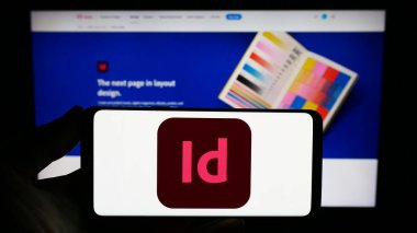 Stuttgart, Almanya - 09-23-2023: Masaüstü yayın yazılımı Adobe InDesign 'in logosuna sahip akıllı telefonu web sitesinin önünde tutan kişi. Telefon ekranına odaklan.