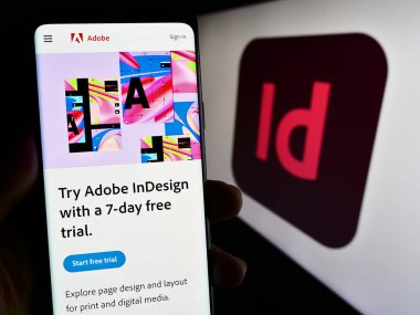 Stuttgart, Almanya - 09-23-2023: Masaüstü yayıncılık yazılımı Adobe InDesign 'in web sayfası olan akıllı telefonu logolu kişi ekranda. Telefon ekranının merkezine odaklan.