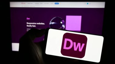 Stuttgart, Almanya - 09-23-2023: Web geliştirme yazılımı Adobe Dreamweaver 'ın logosu olan cep telefonu şirketinin web sayfasının önünde. Telefon ekranına odaklan.