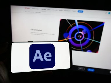 Stuttgart, Almanya - 09-23-2023: Cep telefonu elinde hareket grafik yazılımı logosu olan kişi Adobe After Effects ekranda, web sayfasının önünde. Telefon ekranına odaklan.