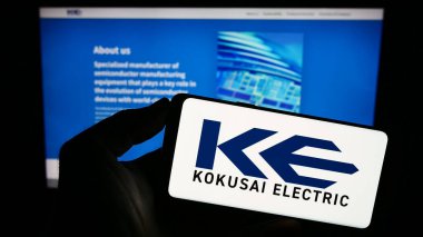 Stuttgart, Almanya - 09-24-2023: Japon şirketi Kokusai Electric Corporation 'ın logosunu elinde tutan kişi web sitesinin önünde ekranda. Telefon ekranına odaklan.