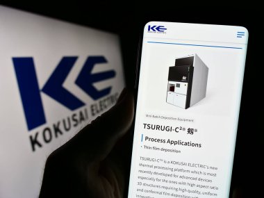 Stuttgart, Germany - 09-24-2023: Person holding cellphone with webpage of Japanese company Kokusai Electric Corporation on screen with logo. Focus on center of phone display. clipart