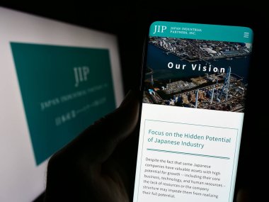 Stuttgart, Almanya - 09-24-2023: Japon Endüstriyel Ortaklar A.Ş. (JIP) adlı şirketin internet sitesiyle cep telefonu elinde bulunan kişi logolu. Telefon ekranının merkezine odaklan.