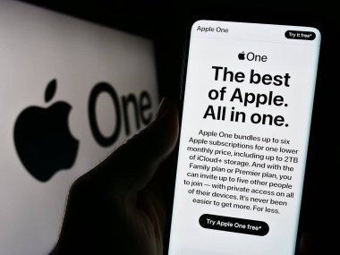 Stuttgart, Almanya - 09-24-2023: Logonun önündeki ekranda abonelik hizmeti Apple One web sayfası ile akıllı telefon tutan kişi. Telefon ekranının merkezine odaklan.