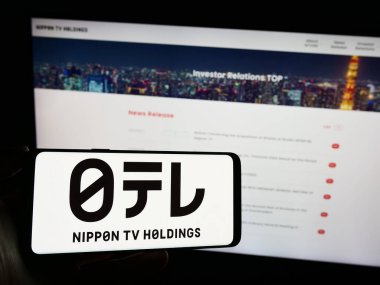 Stuttgart, Germany - 09-24-2023: Person holding smartphone with logo of media company Nippon Television Holdings Inc. on screen in front of website. Focus on phone display. clipart