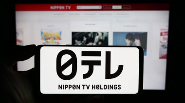 Stuttgart, Germany - 09-24-2023: Person holding cellphone with logo of media company Nippon Television Holdings Inc. on screen in front of webpage. Focus on phone display. clipart