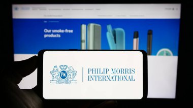 Stuttgart, Almanya - 08-06-2023: ABD 'li Philip Morris International Inc. şirketinin logosuyla cep telefonu sahibi kişi iş sayfasının önünde ekranda. Telefon ekranına odaklan.