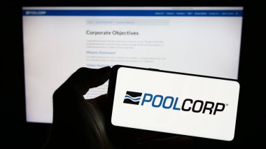 Stuttgart, Almanya - 08-06-2023: ABD 'li Pool Corporation (POOLCORP) şirketinin logosuyla cep telefonu sahibi kişi iş sayfasının önünde ekranda. Telefon ekranına odaklan.