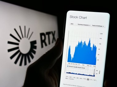 Stuttgart, Germany - 08-06-2023: Person holding cellphone with website of US aerospace and defense company RTX Corporation on screen with logo. Focus on center of phone display. clipart