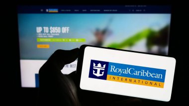 Stuttgart, Almanya - 08-07-2023: Royal Caribbean International (RCI) şirketinin logosuyla cep telefonu sahibi kişi iş sayfasının önünde ekranda. Telefon ekranına odaklan.