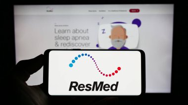 Stuttgart, Germany - 08-07-2023: Person holding cellphone with logo of US medical equipment company ResMed Inc. on screen in front of business webpage. Focus on phone display. clipart