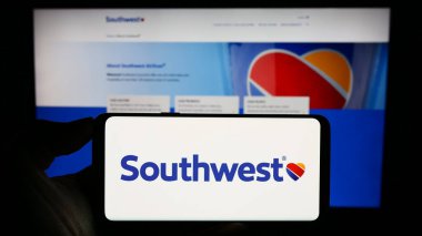 Stuttgart, Germany - 08-08-2023: Person holding smartphone with logo of US airline company Southwest Airlines Co. on screen in front of website. Focus on phone display. clipart