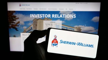 Stuttgart, Germany - 08-08-2023: Person holding cellphone with logo of US paints business The Sherwin-Williams Company on screen in front of webpage. Focus on phone display. clipart