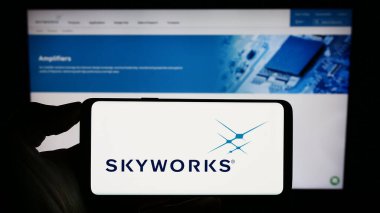 Stuttgart, Almanya - 08-08-2023: İnternet sayfası önünde ekranda ABD 'li yarı iletken şirket Skyworks Solutions Inc.' in logosunun bulunduğu cep telefonu sahibi kişi. Telefon ekranına odaklan.