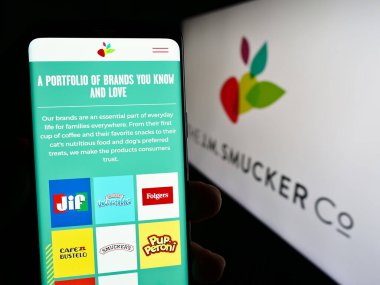 Stuttgart, Almanya - 08-08-2023: Amerikan Gıda İşletmeleri web sayfası ile akıllı telefon tutan kişi The J.M. Smucker Şirketi logonun önünde ekranda. Telefon ekranının merkezine odaklan.