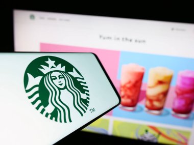 Stuttgart, Germany - 08-09-2023: Smartphone with logo of American coffeehouse company Starbucks Corporation on screen in front of website. Focus on center-right of phone display. clipart