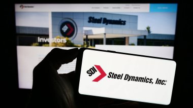Stuttgart, Almanya - 08-09-2023: ABD 'li çelik üreticisi Steel Dynamics Inc.' in logosuyla cep telefonu sahibi kişi iş sayfasının önünde ekranda. Telefon ekranına odaklan.