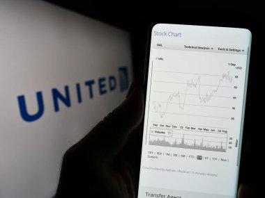 Stuttgart, Germany - 08-11-2023: Person holding cellphone with webpage of US company United Airlines Holdings Inc. on screen in front of logo. Focus on center of phone display. clipart