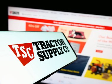 Stuttgart, Germany - 08-11-2023: Cellphone with logo of American retail business Tractor Supply Company on screen in front of website. Focus on center-left of phone display. clipart