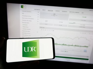 Stuttgart, Almanya - 08-11-2023: Amerikan emlak şirketi UDR Inc. 'nin logosunun bulunduğu cep telefonu sahibi kişi iş sayfasının önünde ekranda. Telefon ekranına odaklan.