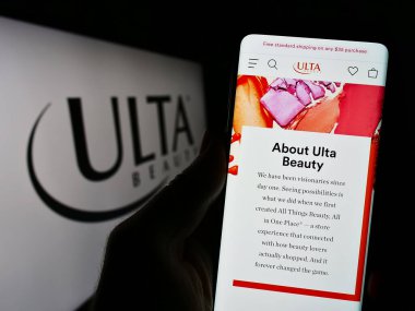 Stuttgart, Germany - 08-11-2023: Person holding smartphone with webpage of US cosmetics retail company Ulta Beauty Inc. on screen with logo. Focus on center of phone display. clipart