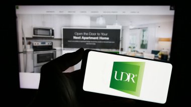 Stuttgart, Almanya - 08-11-2023: ABD 'li emlak şirketi UDR Inc.' nin logosuyla cep telefonu sahibi kişi iş sayfasının önünde ekranda. Telefon ekranına odaklan.