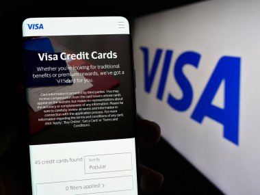 Stuttgart, Germany - 08-12-2023: Person holding mobile phone with web page of US payment processing company Visa Inc. on screen in front of logo. Focus on center of phone display. clipart