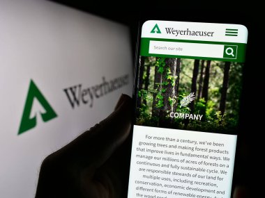 Stuttgart, Almanya - 08-12-2023: ABD Timberland şirketi Weyerhaeuser Company 'nin logolu web sayfası ile akıllı telefonu elinde tutan kişi. Telefon ekranının merkezine odaklan.