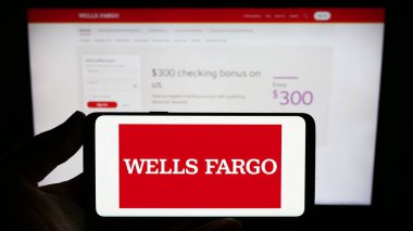 Stuttgart, Germany - 08-12-2023: Person holding smartphone with logo of US financial business Wells Fargo Company on screen in front of website. Focus on phone display. clipart