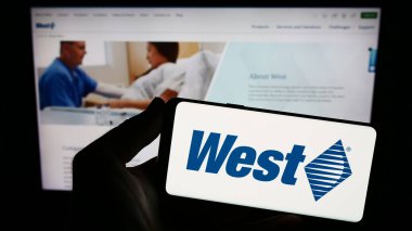 Stuttgart, Almanya - 08-12-2023: Web sitesi önünde ekranda ABD 'li West Pharmaceutical Services Inc.' in logosunu taşıyan kişi. Telefon ekranına odaklan.