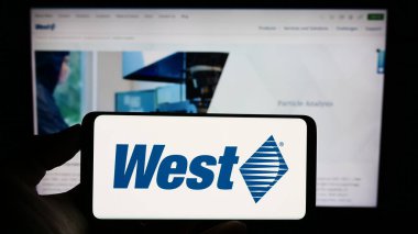 Stuttgart, Almanya - 08-12-2023: Web sayfasındaki ekranda, üzerinde West Pharmaceutical Services Inc. 'in logosu bulunan cep telefonu sahibi kişi. Telefon ekranına odaklan.